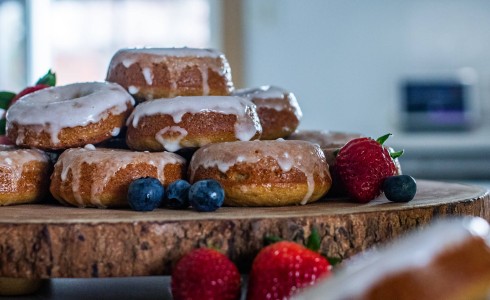 Recipe Blog - Peach Cider Donuts - Side shot, pile of iced donuts on a wooden tray with berries for garnish